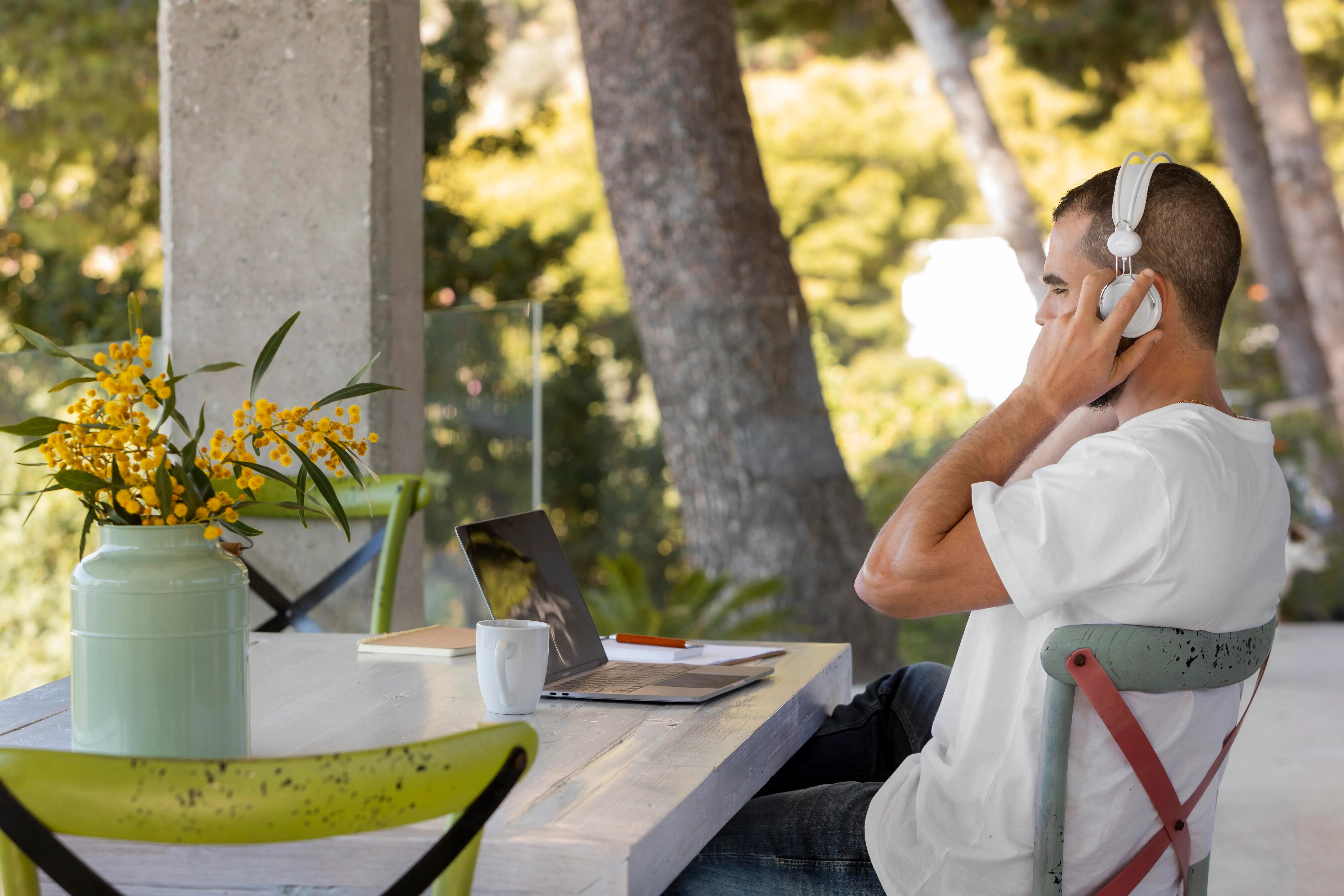 En la fotografía, hombre trabaja en su laptop mientras está sentado en una silla acogedora en el patio de su casa, rodeado de naturaleza.