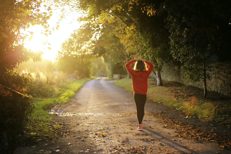 A woman putting her hair up before running down a gravel road at sunset.