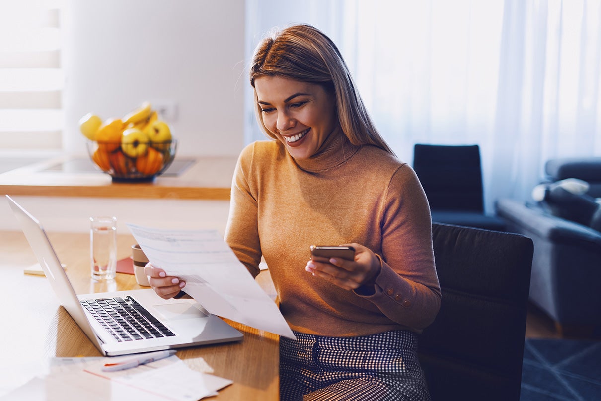 Woman sitting at desk with laptop while reviewing a spreadsheet