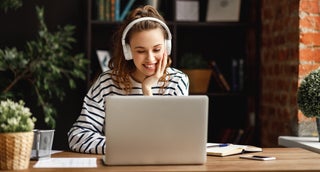 Woman wearing headphones smiles at laptop