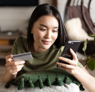 Young woman looks at phone with card in hand