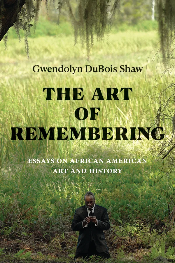 Cover of The Art of Remembering: Essays on African American Art and History by Gwendolyn DuBois Shaw. Cover features a photograph of an African American man kneeling in a suit in the foreground. The man kneels in a field of tall, green grass with whispy vines hanging above his head. The field extends far into the background, revealing a large grassy plain.