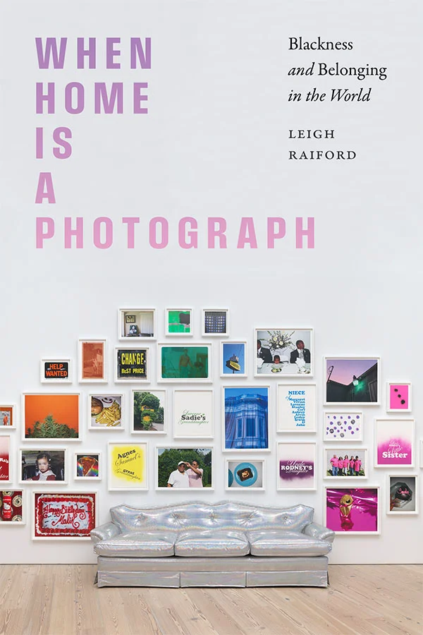 Cover of When Home Is a Photograph features a silver iridescent couch on a hardwood floor surrounded by a gallery wall of framed artwork and photographs on a white wall. The art is arranged by color to create a rainbow.