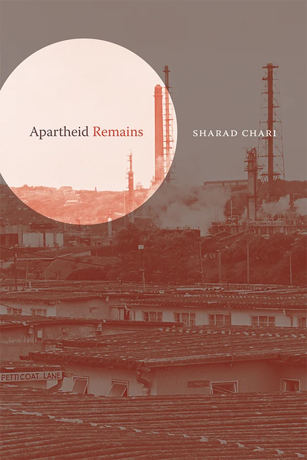 Cover of Apartheid Remains by Sharad Chari. A photograph of a cityscape is featured on the cover. The photograph is edited with a red-hued filter. Smoke comes out of a factory in the background. The entire cover is dimmed except for a circle at the top, left corner that is bright and highlights the title text.