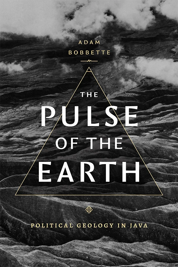 Cover of The Pulse of the Earth: Political Geology in Java by Adam Bobbette. Cover is a black and white photo of a rocky field, with clouds drifting over the field. In the center of the cover is a translucent dark gray triangle outlined in gold. Over the triangle is the title, and above and beneath it is the author information and subtitle.