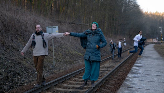 The actors walk down train tracks.