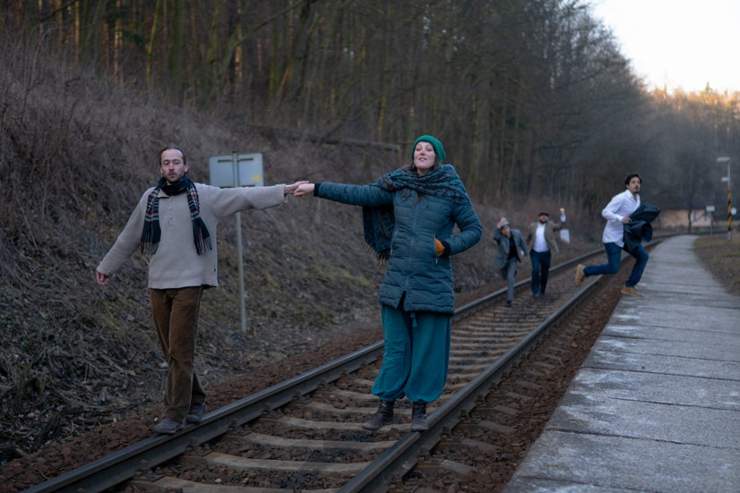 The actors walk down train tracks.