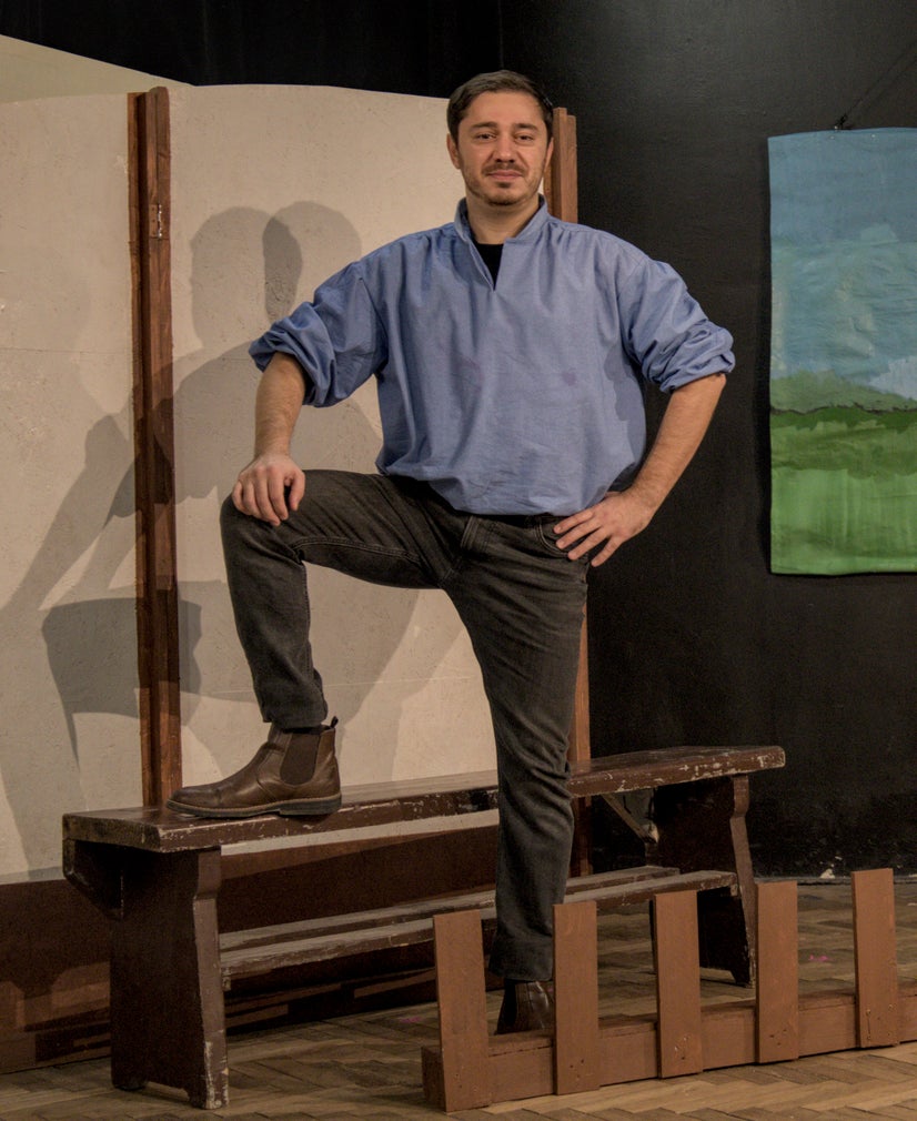 A man in a blue shirt standing with one foot up on a bench in front of a small fence.