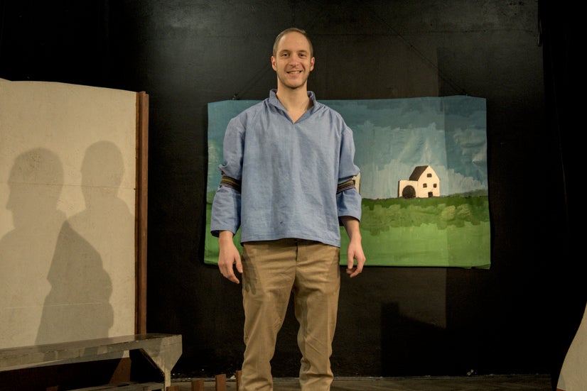 A smiling man in an old-fashioned blue shirt with garters on his arms.