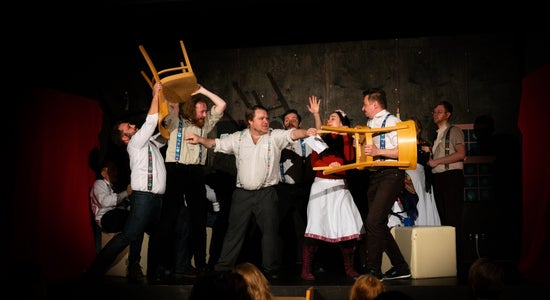 Actors on stage waving chairs at each other while others try to break up the stage fight.
