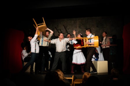 Actors on stage waving chairs at each other while others try to break up the stage fight.