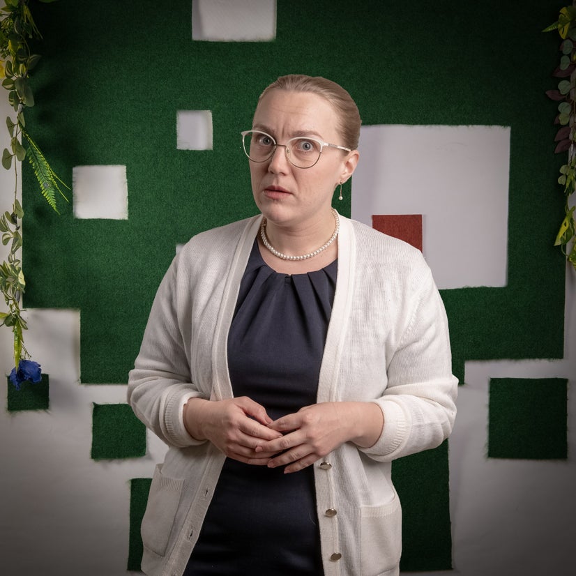 An actor wearing pearls stares balefully at the camera.