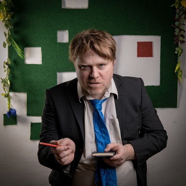 An actor with a notebook looks at the camera.