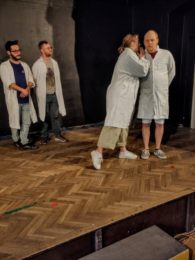 A distinguished professor sharing a secret with Sigelius as his assistants look on.