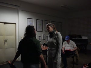 A man and woman argue in the middle of a room while another man reads a script nearby.