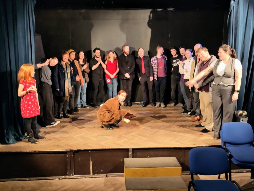 I wonder what she found there. One actor picking something off the center stage while many others look on around her.