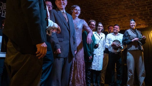 Various people in costume stand in a line on a stage.