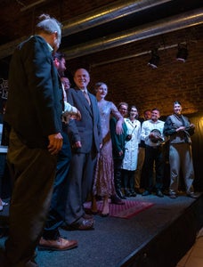 Various people in costume stand in a line on a stage.