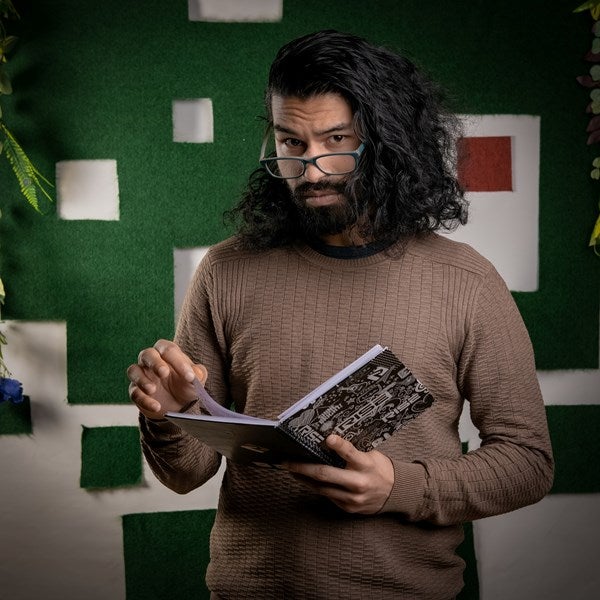 An actor looks over his glasses at the camera while holding a notebook.