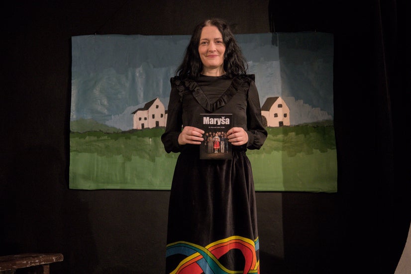 A woman in a black dress smiling and holding a copy of the book Maryša.