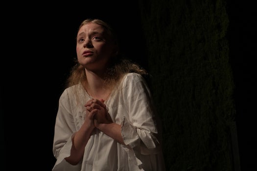 A woman in a flowing white shirt prays while looking up.