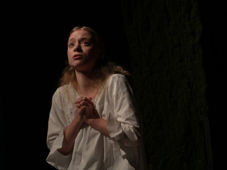 A woman in a flowing white shirt prays while looking up.