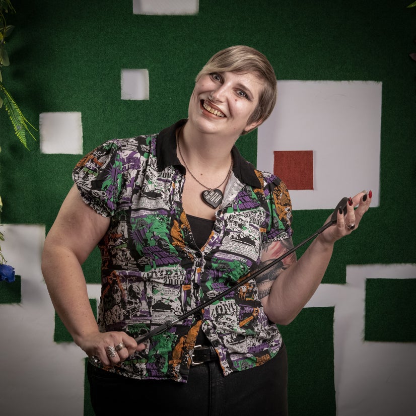 A smiling woman smacks a riding crop on her hand.