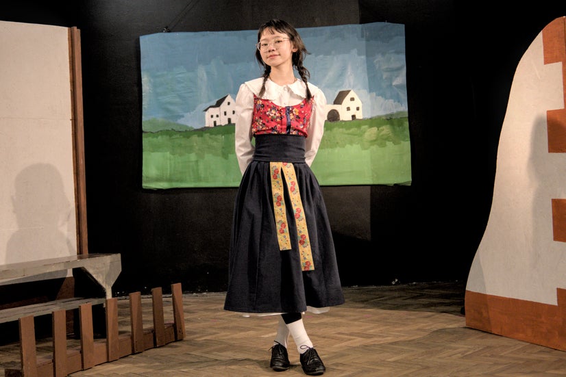 A woman in a white and red shirt and a long black skirt standing with her legs crossed.