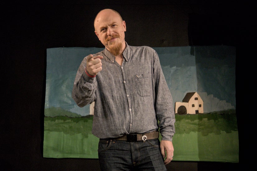 A man in a blue dress shirt looking and pointing at the camera.