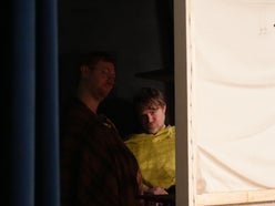 Two men (Adam and Jack) behind a curtain backstage. Jack is staring at the camera.