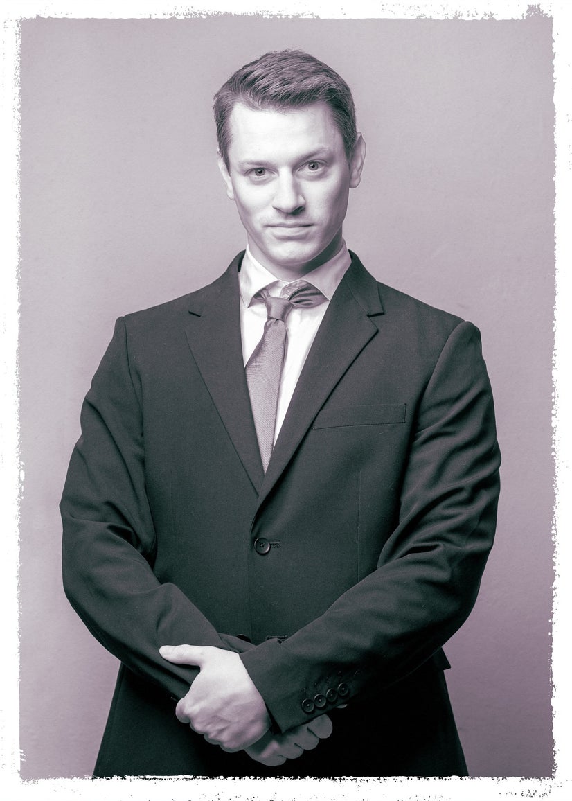 A black-and-white photo of a man in a suit and tie with his arms clasped in front of him.