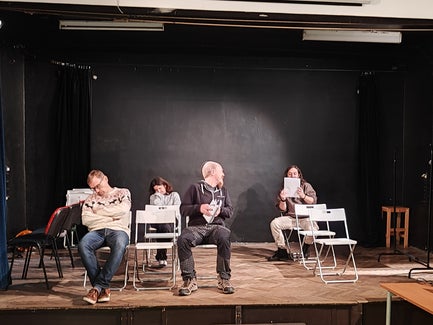 A man sitting in a chair looks behind him while another man and a woman sleep in their chairs.