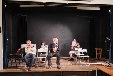 A man sitting in a chair looks behind him while another man and a woman sleep in their chairs.
