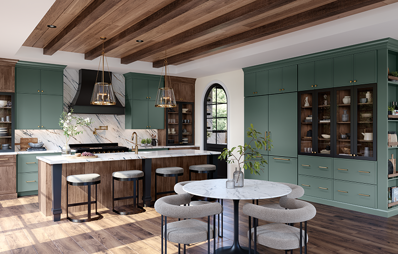An open kitchen concept displays the counters and kitchen island to the left, set with modern black iron barstools. To the right we see a deep sage green wall of custom cabinetry, with glass section for easy viewing of items on display, and a round marble table set with four chairs in the foreground.