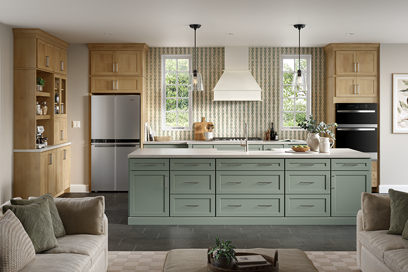 From the view of the living room, there is a sage-green kitchen island with plenty of drawers for storage and neutral grey flooring, creating a soft focal point in the otherwise neutral-toned kitchen with natural wooden cabinetry.