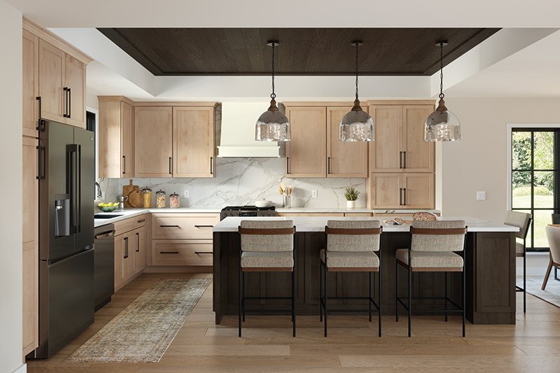 A kitchen in neutral wood tones, with lighter kitchen cabinets, and darker wood kitchen island. A soft touch of natural lighting comes in from the windows on the left, and the room opens up to the right.