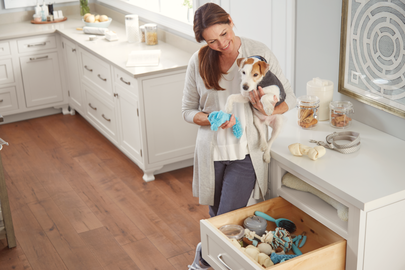 A woman with a dog in her kitchen using animal-specific storage cabinets.