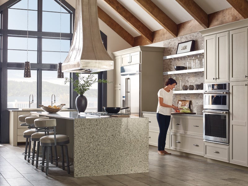 A woman cooking in a large open kitchen with a marble island and wood kitchen cabinets.