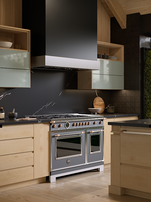 This is a focused shot of a high-end kitchen oven range with sleek modern hood in matching dark charcoal grey. The backsplash is a neutral dark grey, and all surrounding cabinetry is a light natural wood tone.