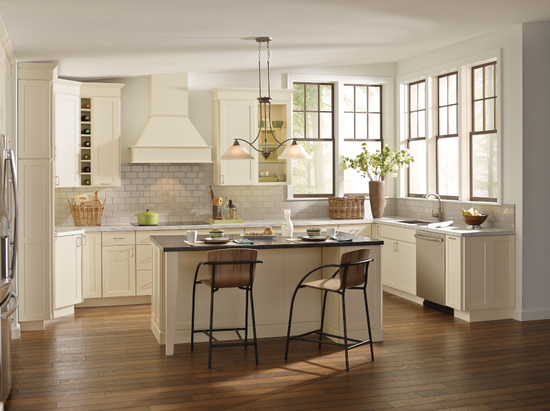This kitchen utilizes a cream color palette, with off-white tile backplash, cream-colored cabinetry, and touches of woven textures in baskets and on the back of the barstools for an overall soft look, as natural lighting comes in from the right of the kitchen.