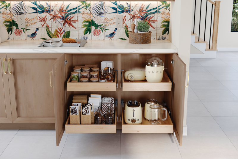 Lower kitchen cabinets are opened to reveal roll trays behind the doors. Two trays pull out on the right and the left side, with one tray above the other, stocked with pantry items and kitchen gadgets.