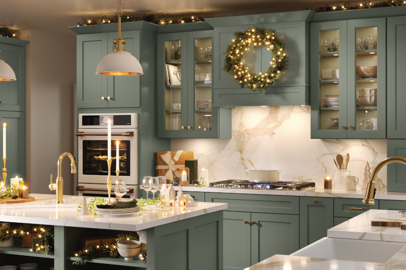 A kitchen decorated for the holiday season with a wreath and string lights, with sage green cabinets.