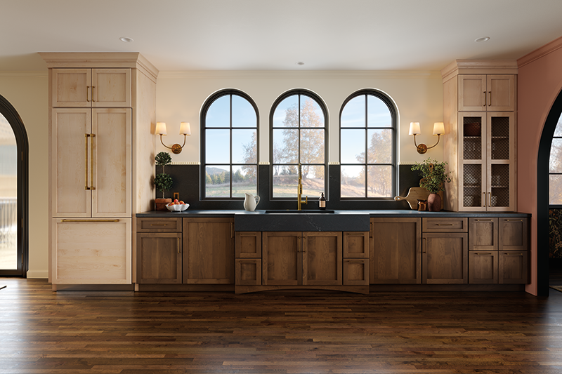 This open kitchen design features three arched windows at the center, with kitchen sink and dark-toned countertop aligned with this architectural detail. Dark wood lower cabinets, earthy-toned and textures walls, and a deep natural stained wooden floor create a bold statement. Sconces rest on both sides of the windows.