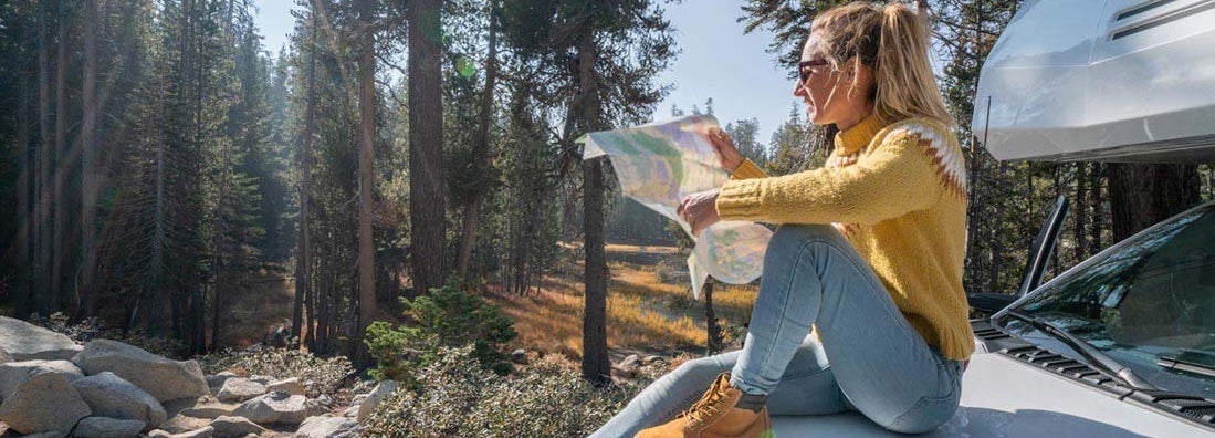 Woman sitting on motorhome hood checking road map for directions. Find Tennessee RV Insurance. 