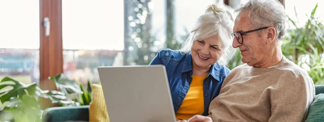 Senior couple using laptop while sitting on sofa in living room at home. Life Insurance: Cash Value & Surrender.
