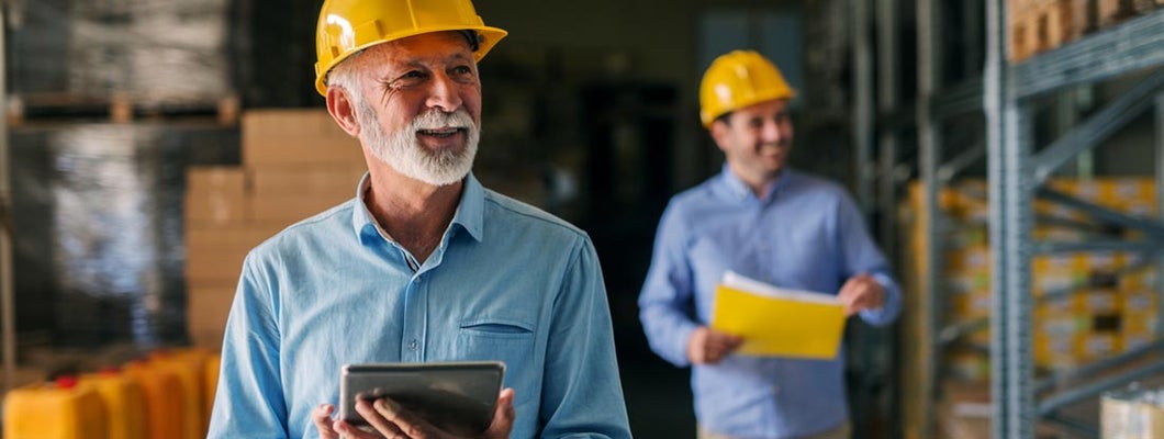 Business owner and employee walking through their warehouse with helmets on their heads. Workers' Compensation Insurance Cost.