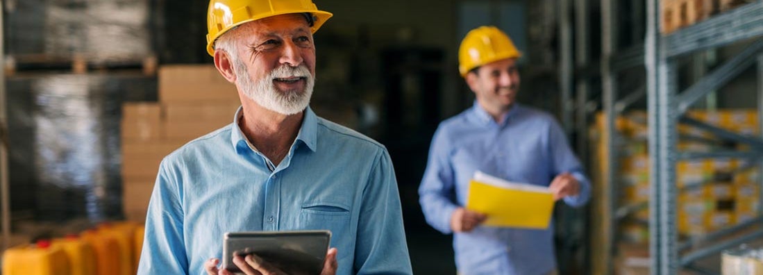 Business owner and employee walking through their warehouse with helmets on their heads. Workers' Compensation Insurance Cost.