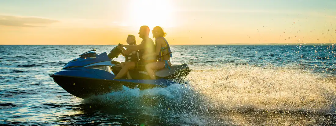 Family having fun riding a person watercraft on the sea in the sunset. Find Wave Runner Insurance.