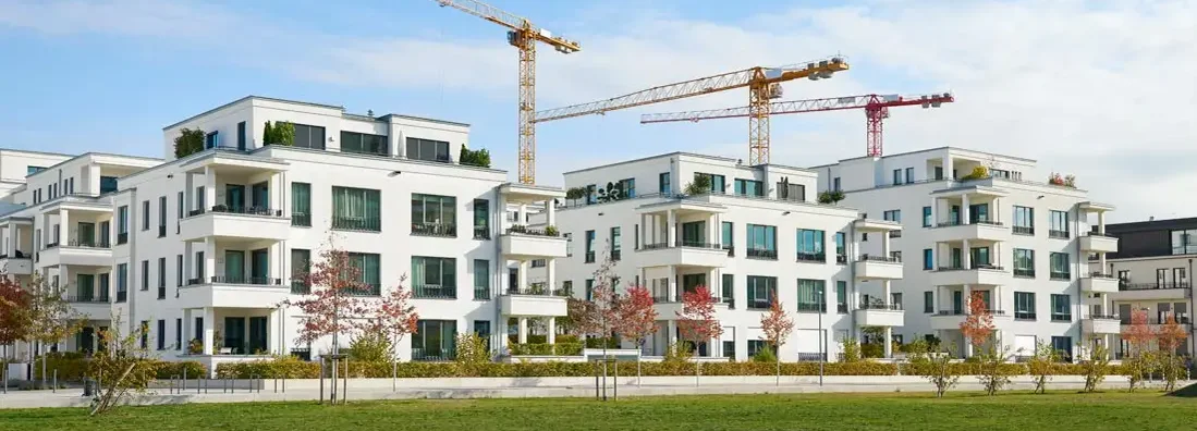 Brand new luxury townhouses with three cranes of a construction area behind the buildings. Find Condo Construction Insurance.