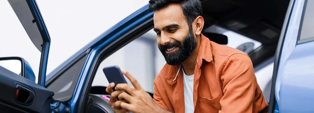 Man Using Phone Sitting In Auto With Opened Door. Is Car Insurance Always Required?